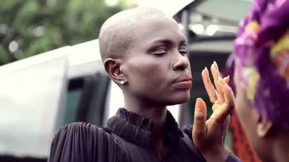 Ajuma Nasenyana assistant applying makeup outdoors on set