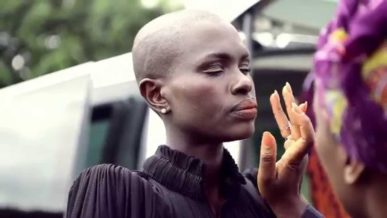 Ajuma Nasenyana assistant applying makeup outdoors on set