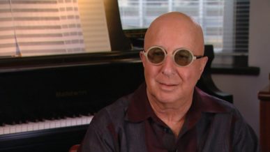 Paul Shaffer being interviewed at home wearing round glasses beside his piano