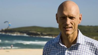 Peter Garrett at a beach with parasailer in background