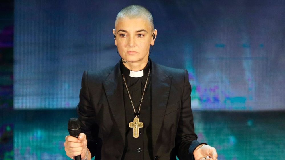 Sinead O'Connor wearing a Catholic priests uniform with shaved head hair